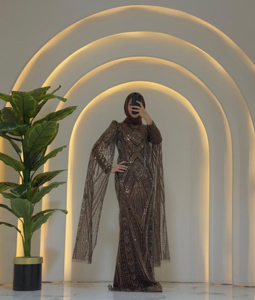 Orjinal Kristal taş Ön yüzeyde V-şekilli ve zikzaklı Art Deco tarzı geometrik desenler hakimdir Uzun kolları, omuzlardan yere kadar sarkan, ince tül üzerine işlenmiş pelerin/kanat benzeri bir detayla uzatılmıştır Yüksek yakalı ve uzun Kahverengi  Abiye 44