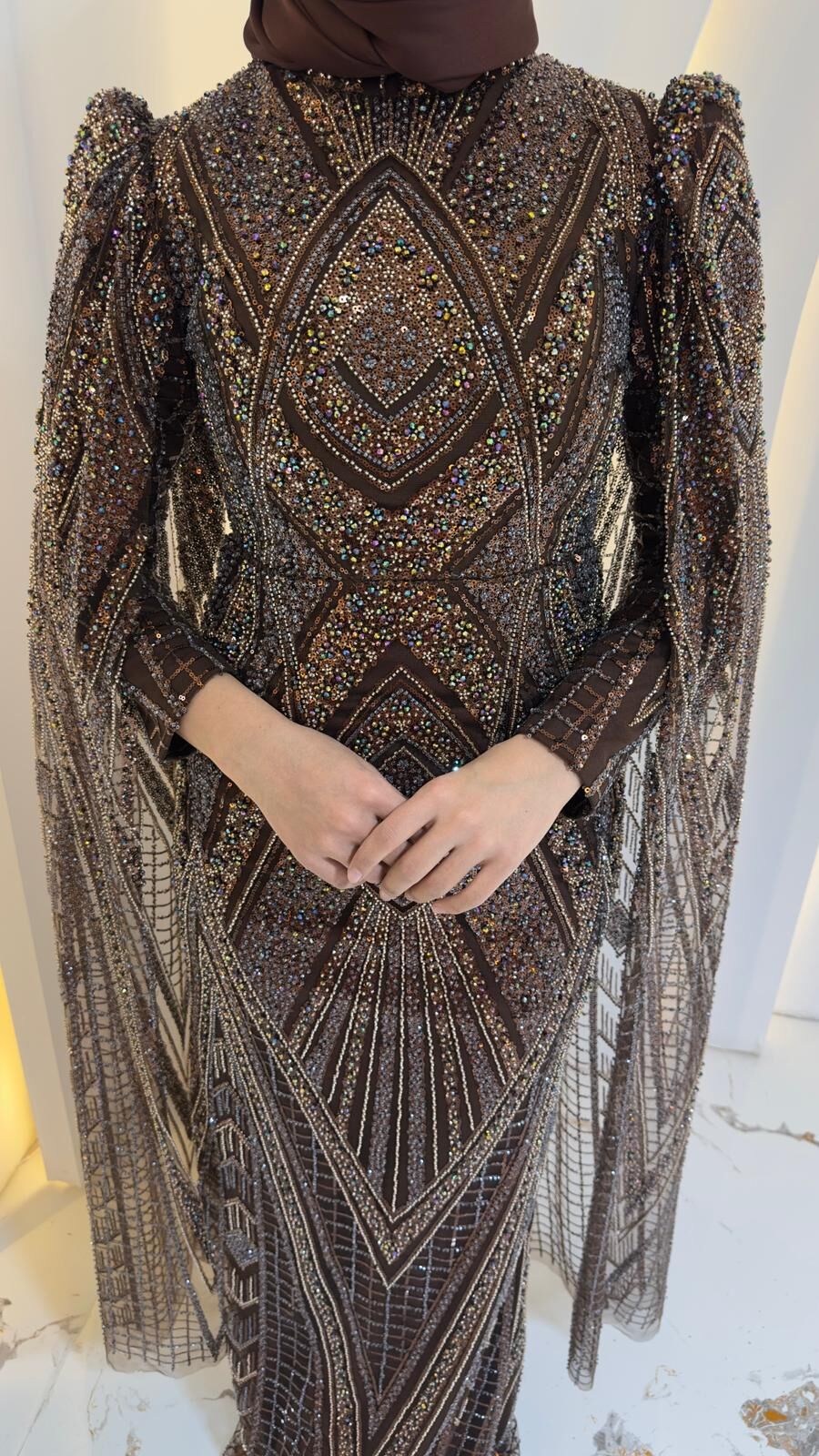 Orjinal Kristal taş Ön yüzeyde V-şekilli ve zikzaklı Art Deco tarzı geometrik desenler hakimdir Uzun kolları, omuzlardan yere kadar sarkan, ince tül üzerine işlenmiş pelerin/kanat benzeri bir detayla uzatılmıştır Yüksek yakalı ve uzun Kahverengi  Abiye 44