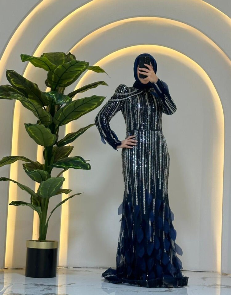 Elbisenin gövdesi boyunca uzanan dikey çizgisel pullu ve boncuklu işlemeler Omuzlardan sarkan inci veya boncuk zincirlerden Yüksek yakalı ve uzun kollu Lacivert Abiye 44