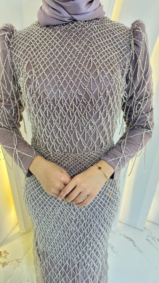 Baştan aşağıya püskül ve boncuk işlemelerle (saçaklı görünümde) süslenmiştir Omuz kısımları hafif kabartmalı/vatkalı yakası yüksek kesimdir Lila Abiye 44