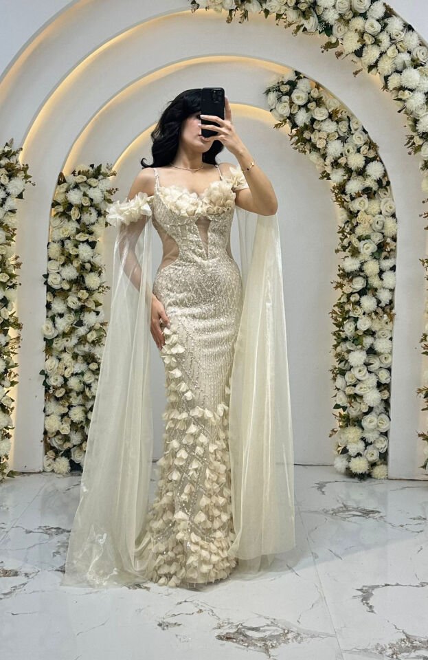 Omuzlardan başlayıp yere kadar inen, tül veya organze kumaştan uzun pelerin/kanatlara sahiptir. Korsaj ve etek kısmında, üç boyutlu çiçek aplikeleri ve incilerle yoğun Krem Abiye 42