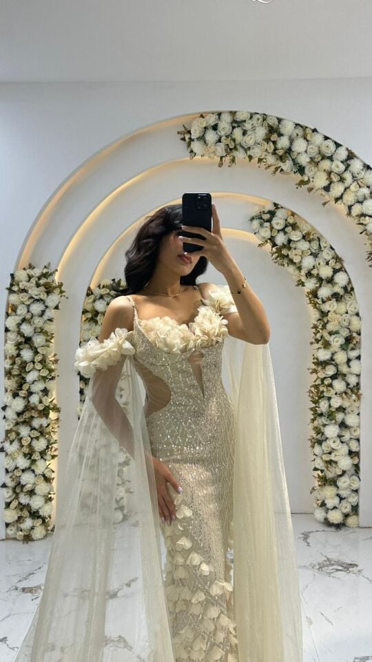 Omuzlardan başlayıp yere kadar inen, tül veya organze kumaştan uzun pelerin/kanatlara sahiptir. Korsaj ve etek kısmında, üç boyutlu çiçek aplikeleri ve incilerle yoğun Krem Abiye 42