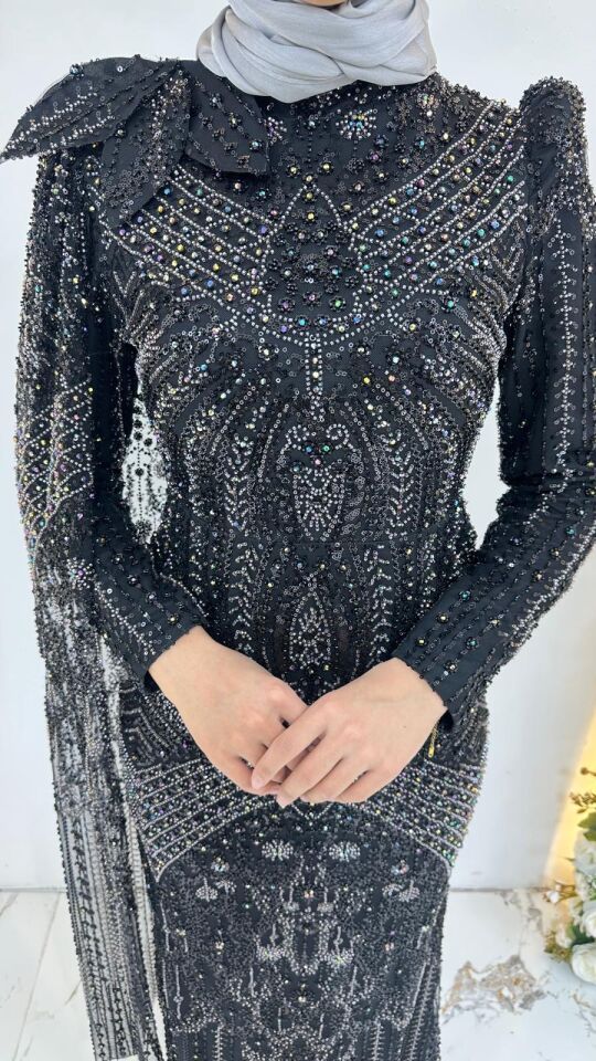 Siyah kumaş üzerine yoğun kristal boncuk, payet ve taş işlemeli Omuz kısmında büyük bir fiyonk Uzun kollu, hakim yakalı ve vücuda oturan balık zarif Siyah Tesettür Abiye 44