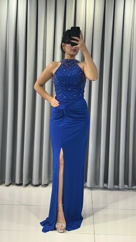 Halter yaka (yüksek, boyundan bağlamalı)Yoğun boncuk ve taş işlemeli (parlak/ışıltılı) Vücuda oturan, yüksek yırtmaçlı uzun etek Yırtmacın hemen üstünde büzgülü/düğüm görünümlü  Mavi Abiye 42