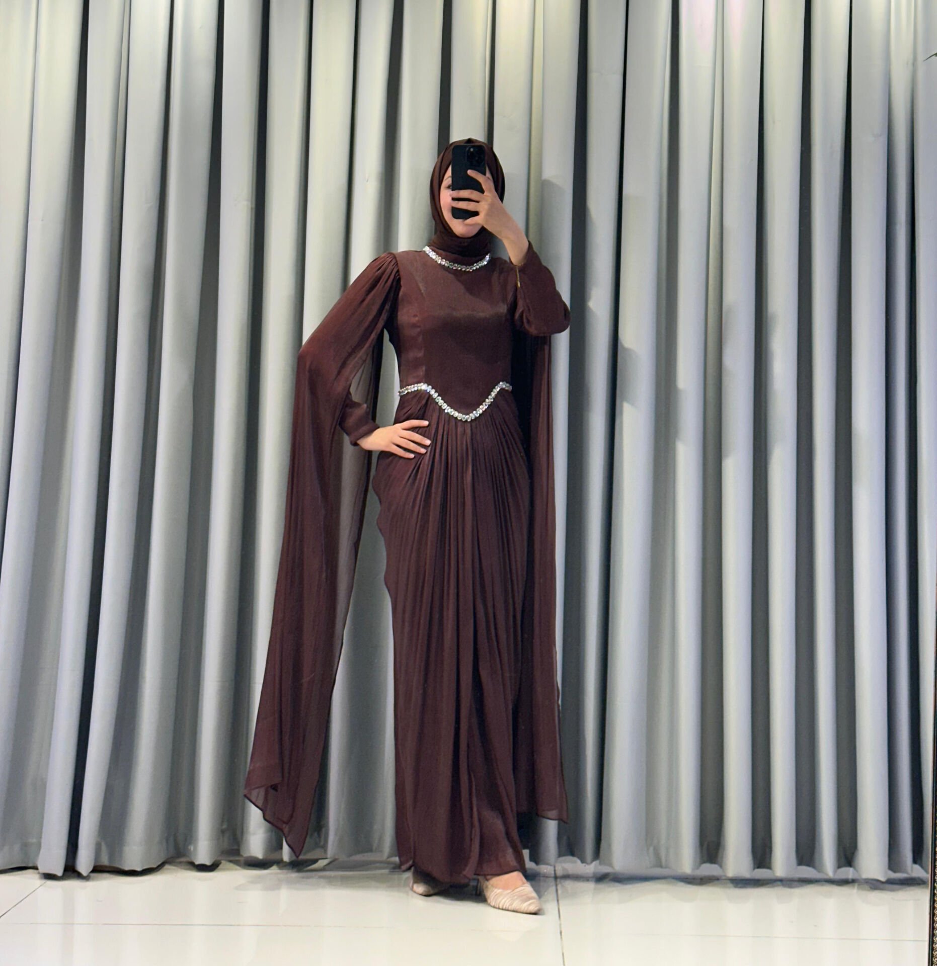 Uzun pelerin kollu, taş detaylı kemerli ve pileli Kahverengi Tesettür Abiye elbisedir. 44