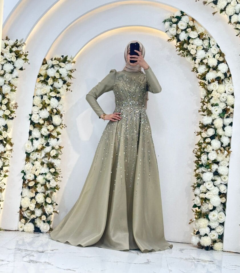 Bel kısmından yukarı ve aşağı doğru yayılan ''ışın'' formunda, göz alıcı payet ve taş işlemeleri mevcuttur Uzun kollu, hakim yakalı ve hafif kabarık Haki Yeşili Tesettür Abiye 44