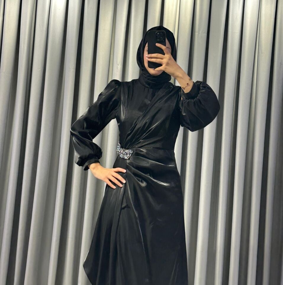 Uzun kollu, saten kumaştan yapılmış omuzları kabarık/vatkalı ve belinde taşlı, dekoratif bir broş detayına sahiptir Eteği, önden drapeli ve katmanlı bir tasarımla yere kadar uzanmaktadır (Siyah Abiye) 44