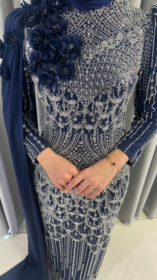 Baştan ayağa boncuk ve pul işlemeleri ile yoğun süslemeli Yüksek yaka Omuzdan başlayıp bele ve yere kadar uzanan, 3D çiçek aplikeleriyle süslü uzun bir şal/pelerin detayı bulunan Vücuda oturan, balık model Lacivert Abiye 44